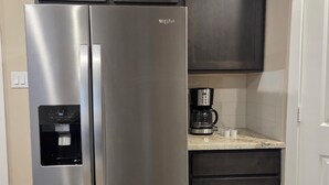 Un réfrigérateur en acier inoxydable doté d’un distributeur d’eau, de meubles de couleur sombre, d’une machine à café et d’une porte blanche.