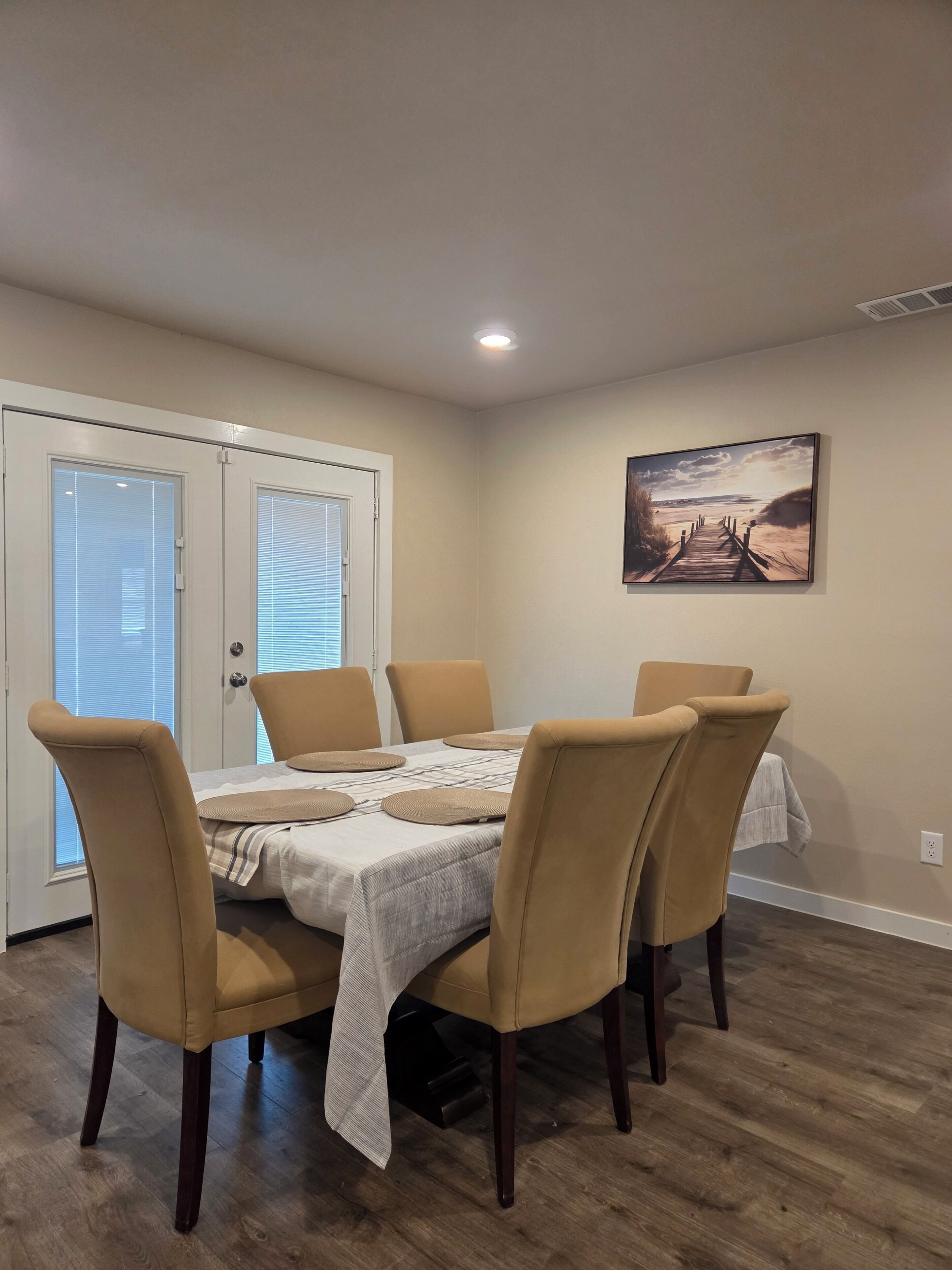 Un coin repas avec une table dressée pour quatre personnes, entourée de quatre chaises. Un tableau est accroché au mur, au-dessus de la table.