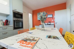 Una cocina moderna con armarios blancos, horno empotrado y comedor con mesa de mármol.