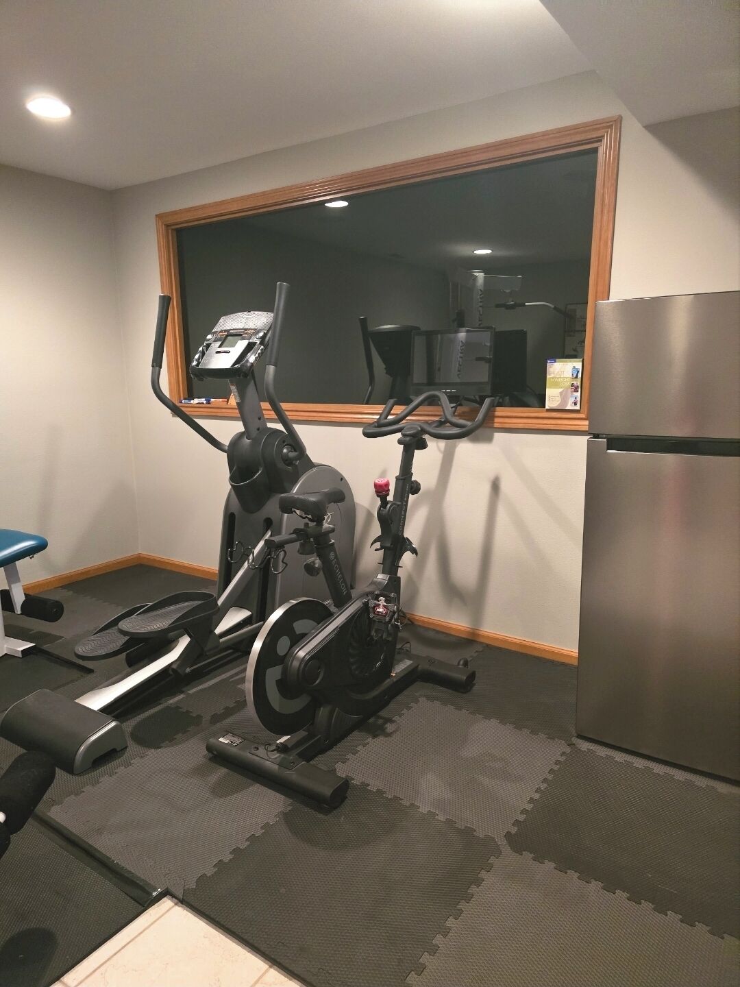 Een sportschool in huis met trainingsapparatuur, een koelkast en een raam.