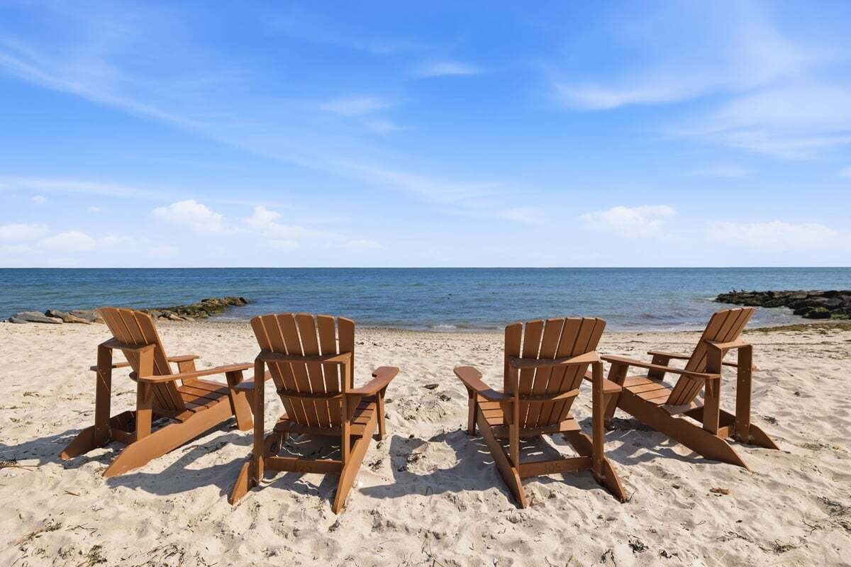 Quattro poltrone da spiaggia in legno disposte su una spiaggia sabbiosa con vista sull'oceano.