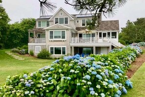 A two-story house with a balcony, surrounded by well-maintained hedges and a lawn.