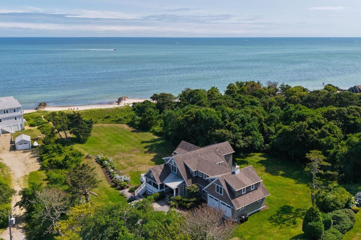 A large house with a garage, surrounded by lush greenery and a beach.