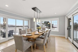 A dining area with a wooden table set for six, large windows, and a view of the outdoors.
