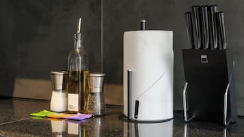 A kitchen counter with a paper towel holder, a salt and pepper shaker, a bottle of olive oil, and a knife block.