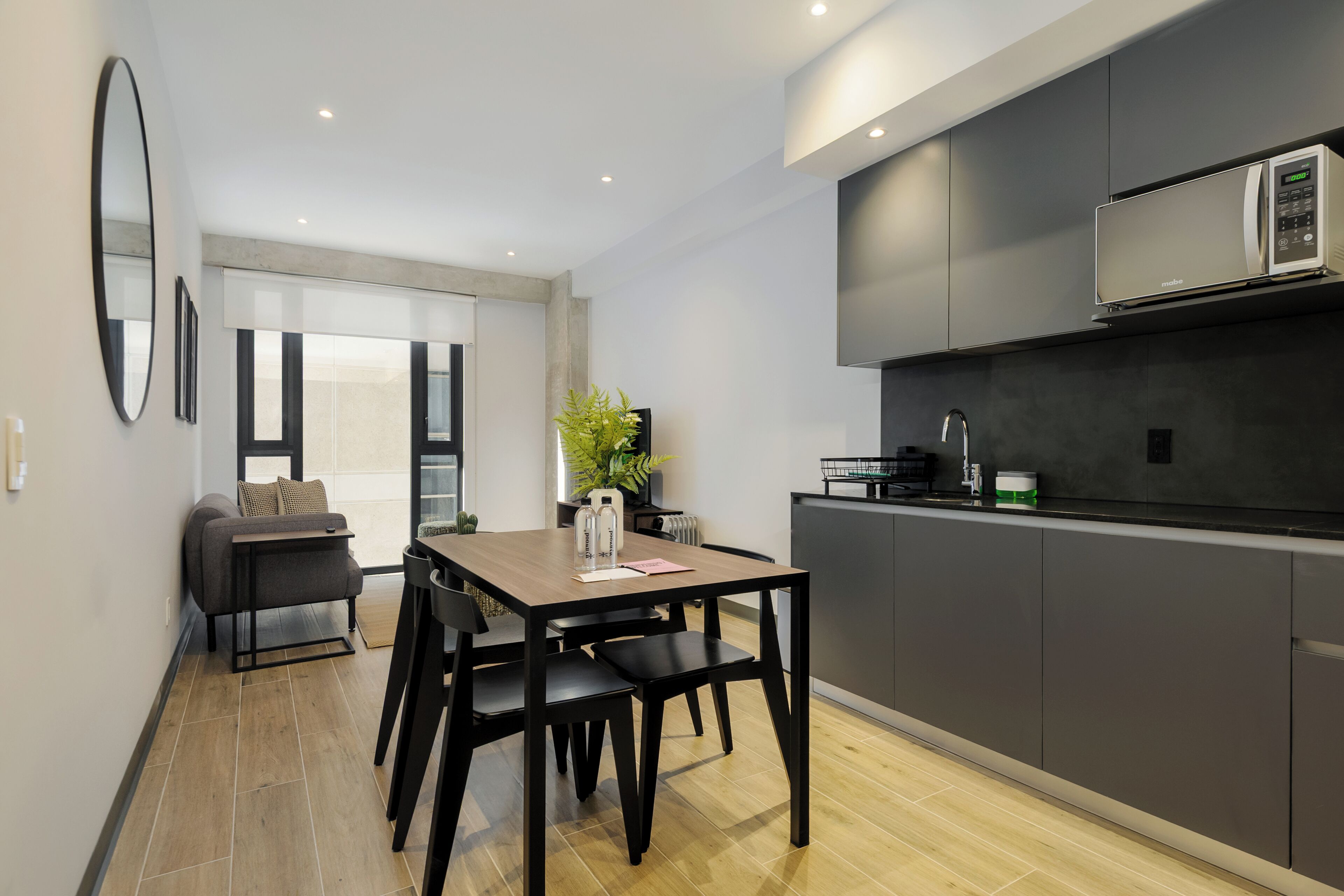A modern kitchen with dark cabinetry, a microwave, and a dining area with a table and chairs.