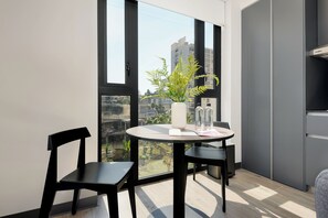 Ein modernes Zimmer mit rundem Tisch und zwei Stühlen, einer Zimmerpflanze und Blick auf eine Stadtkulisse durch große Fenster.