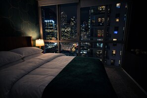 A bedroom with a large bed, a nightstand, a lamp, and a view of a cityscape at night. - Miami Bay Million-Dollar View - Private Condo - Pool - Gym - Sleeps 4 (Miami)