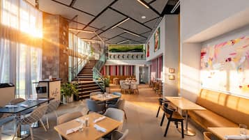 A modern restaurant with a staircase, multiple dining areas, and a large window with natural light.