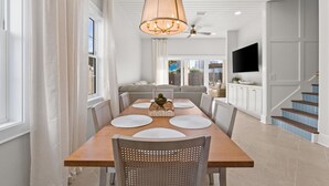 A modern dining room with a wooden table, white chairs, and a large chandelier. - Fall Deals + Snowbird Rates | Coastal Stay Near the Beach (Panama City Beach)