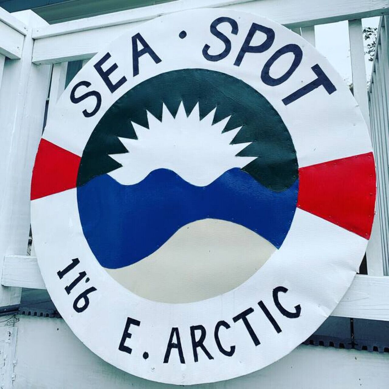 Ein rundes Schild mit dem Text „SEA SPOT 116 E. ARCTIC“ und einer Grafik aus Sonne, Wellen und Land.