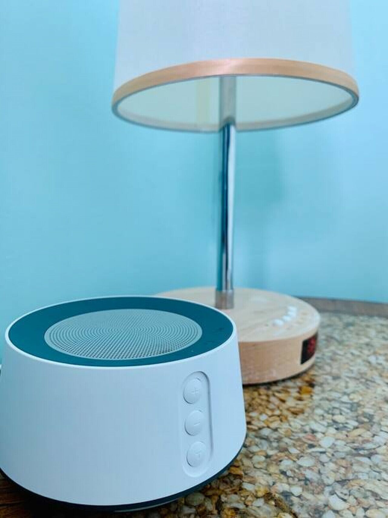 Un haut-parleur blanc, avec un dessus bleu et une base en bois, posé sur un comptoir à motifs.