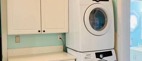 Une buanderie équipée de deux machines à laver et deux sèche-linge superposés, de meubles blancs et d’un meuble ventilé en dessous.