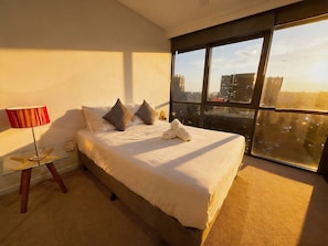 Ein modernes Schlafzimmer mit einem großen Bett, einem Glastisch mit Sterndekoration und Blick auf die Stadt durch große Fenster.