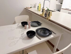 A modern kitchen with white countertops, a white chair, and black dinnerware. - Hope St. 1BR Staycation–Pool, Gym, Sauna +Parking (South Brisbane)