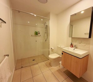 A modern bathroom with a glass-enclosed shower, a toilet, and a sink with a mirror above. - Hope St. 1BR Staycation–Pool, Gym, Sauna +Parking (South Brisbane)