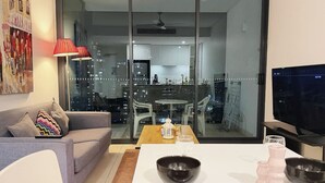 En moderne stue med en sofa, et spisebord med hvid dug og et fjernsyn på et stativ.