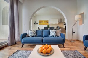 A modern living room with a blue sofa, a coffee table with oranges, and a kitchen in the background. - Spacious Private Apartment With Sunny Balcony (Sliema)