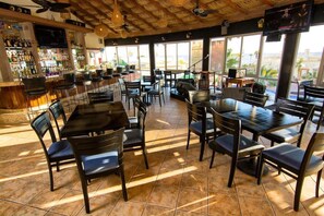 Un restaurant doté d’un bar, de nombreuses tables et chaises, et de grandes fenêtres offrant une vue panoramique.