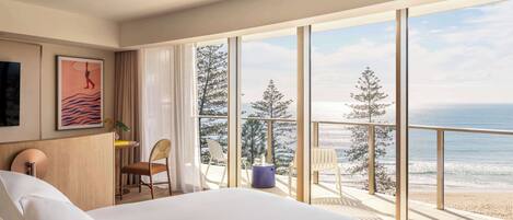 Habitación de hotel con una cama grande, vistas a la playa y un balcón con sillas.