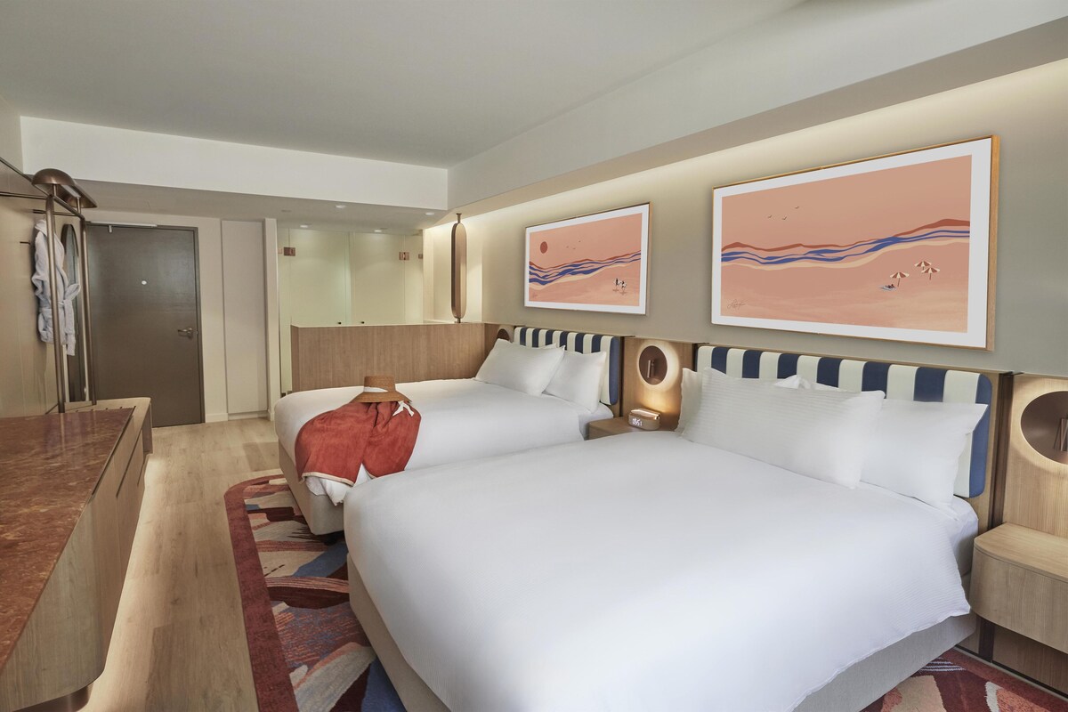 Une chambre d’hôtel avec deux lits, une salle de bain et des œuvres d’art aux murs.