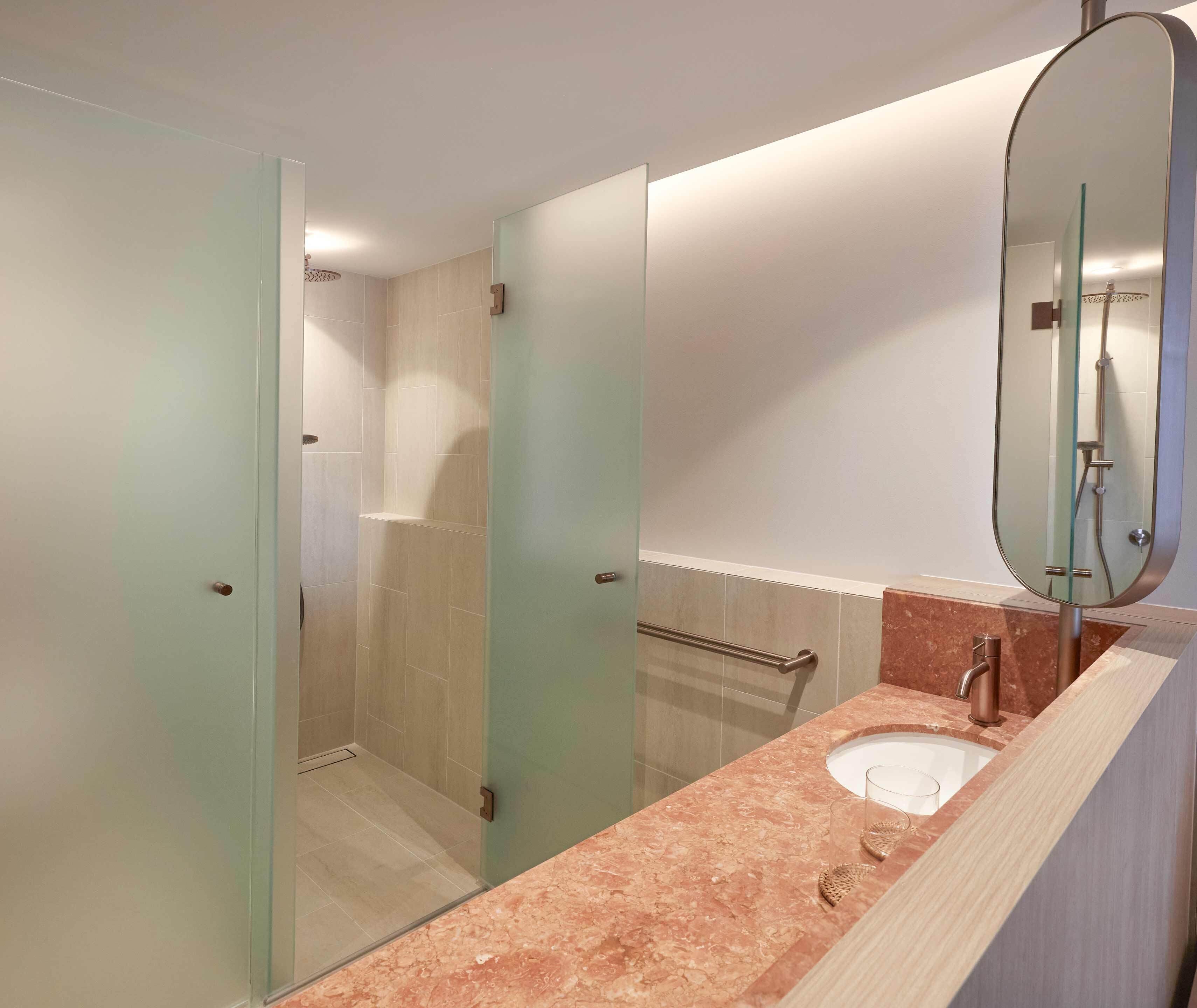 A modern bathroom with a glass shower enclosure, a marble sink, and a large mirror.