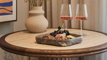 A round wooden table with a marble top, a vase with green foliage, two wine glasses, and a charcuterie board with various meats, cheeses, and grapes.