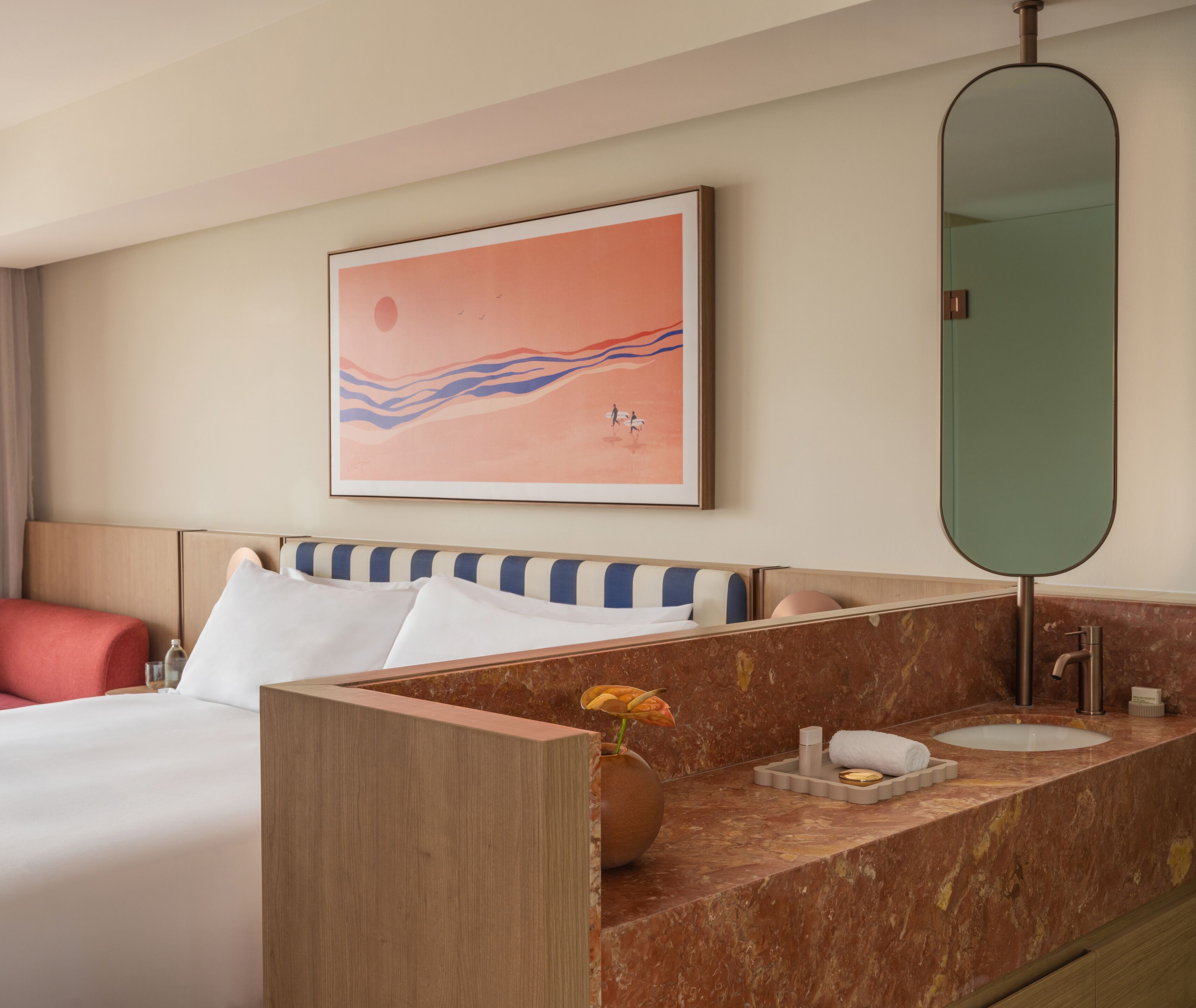 A hotel room with a bed, a bathroom with a marble countertop, a large mirror, and a wall art piece.
