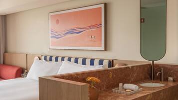 A hotel room with a bed, a bathroom with a marble countertop, a large mirror, and a wall art piece.