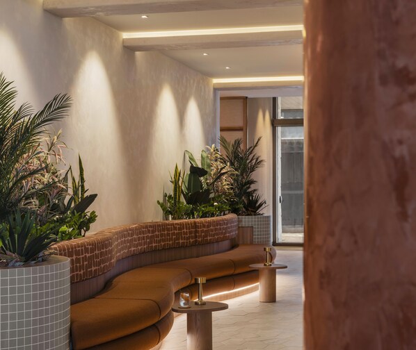 A modern interior with a curved seating area, a glass door leading outside, and potted plants. - Avani Mooloolaba Beach Hotel (Mooloolaba)