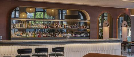 A bar area with a variety of liquor bottles, a seating area with chairs, and a large arched window.
