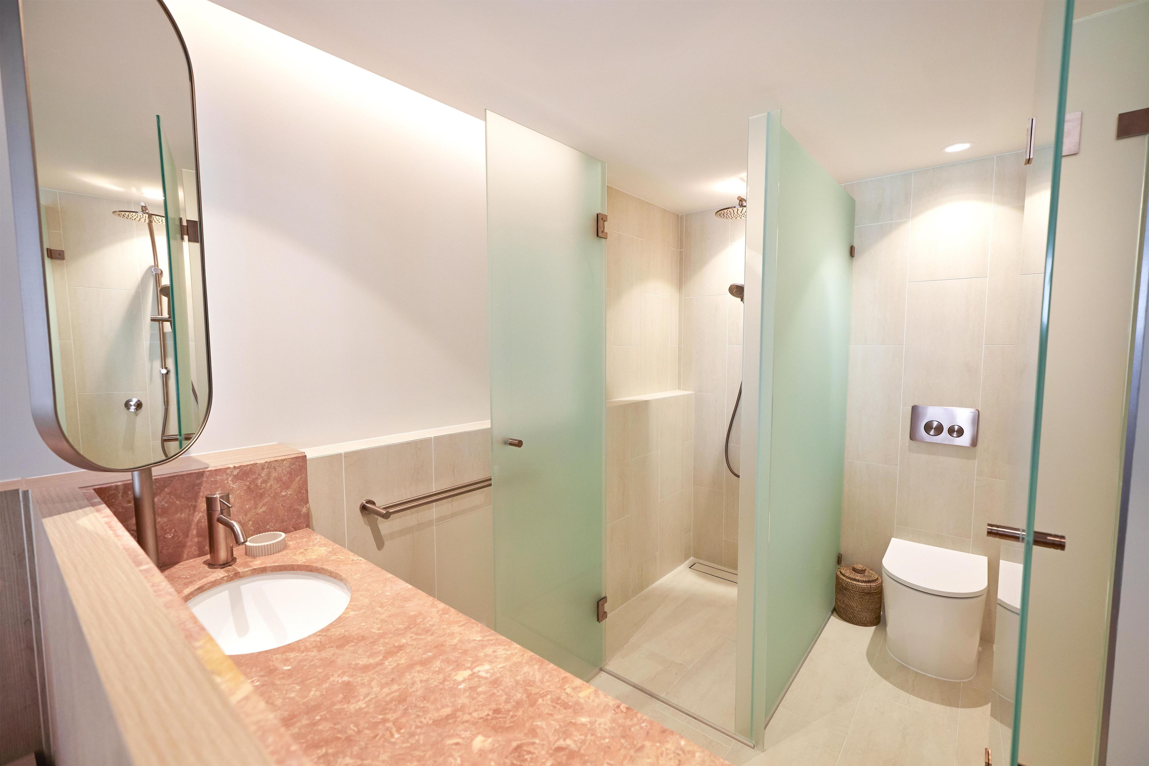 A modern bathroom with a glass-enclosed shower, a sink with a marble countertop, and a toilet.