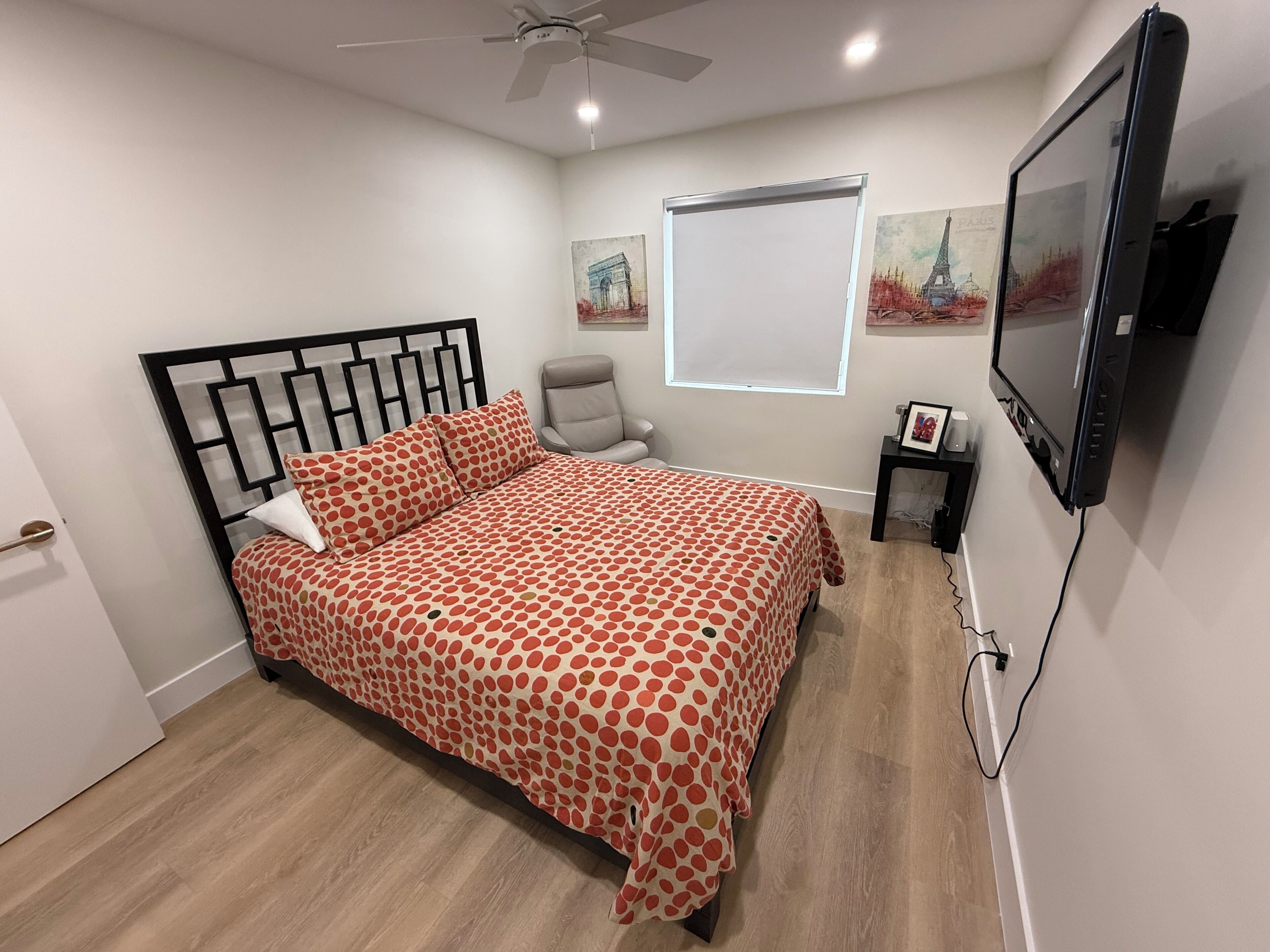 A bedroom with a bed, a chair, a TV, and artwork on the wall.