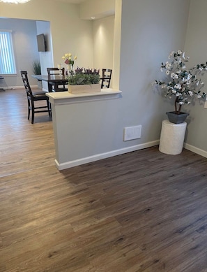 Een moderne woonkamer met een houten vloer, een witte accentmuur, een ingebouwde bank met een plantenbak en een potplant.