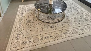 Ett modernt vardagsrum med en grå soffa, ett runt soffbord och en mönstrad matta.