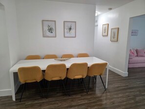 A dining area with a white table and six mustard-colored chairs. There are framed botanical prints on the walls.