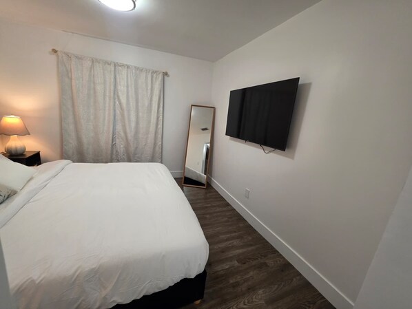 A bedroom with a bed, a bedside lamp, a TV mounted on the wall, and a mirror. - Flamingo Family House - Near Airport
Fabulous 3-bedroom house with AC. (Grove)