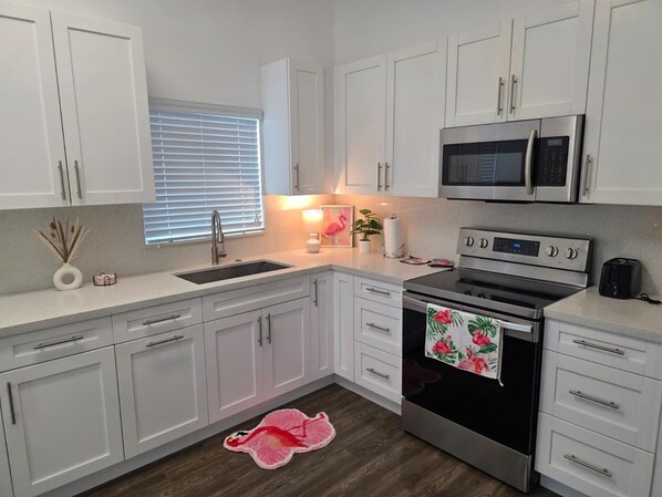 A modern kitchen with white cabinets, a stainless steel oven, a microwave, and a sink.