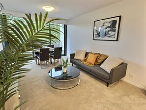 Ein modernes Wohnzimmer mit einem grauen Sofa, einem runden Couchtisch und einer großen Kübelpflanze.
