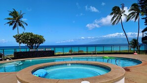 Ein Poolbereich mit Blick auf das Meer, Palmen und einer Liegefläche.