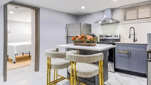 A modern kitchen with a marble countertop, stainless steel appliances, and a small dining area with bar stools.