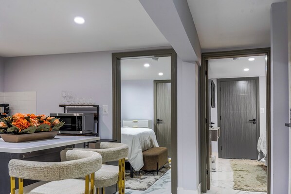 A modern kitchen with a microwave, a bowl of flowers, and a dining area with chairs. - Queens 3-Bedroom Home - The Hideaway (Jamaica)