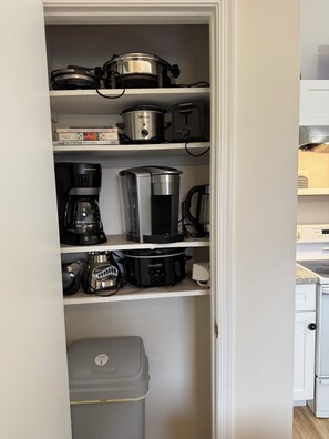 A kitchen with a built-in oven, a coffee maker, a slow cooker, and a trash bin.