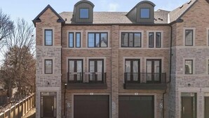A multi-story residential building with a brick facade, multiple windows, and two garage doors. - Luxury Townhome w/ Private Elevator (Newmarket)