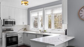 A modern kitchen with white cabinets, a large window, and a marble countertop. - Luxury Townhome w/ Private Elevator (Newmarket)