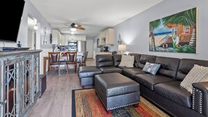 A modern living room with a sectional sofa, a dining area, and a kitchen in the background. - Sea Cloisters II Ocean Front Beach Retreat-101e (North Myrtle Beach)
