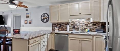 A modern kitchen with beige cabinetry, a marble countertop, a dishwasher, and a refrigerator.