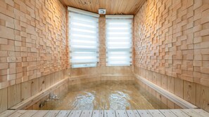 Eine Holzsauna mit zwei großen Fenstern, einem Holzboden und einer mit Fliesen verkleideten Wand.