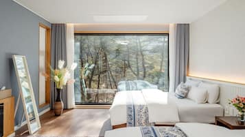 A bedroom with a large window, two beds, a bedside table, and a mirror.