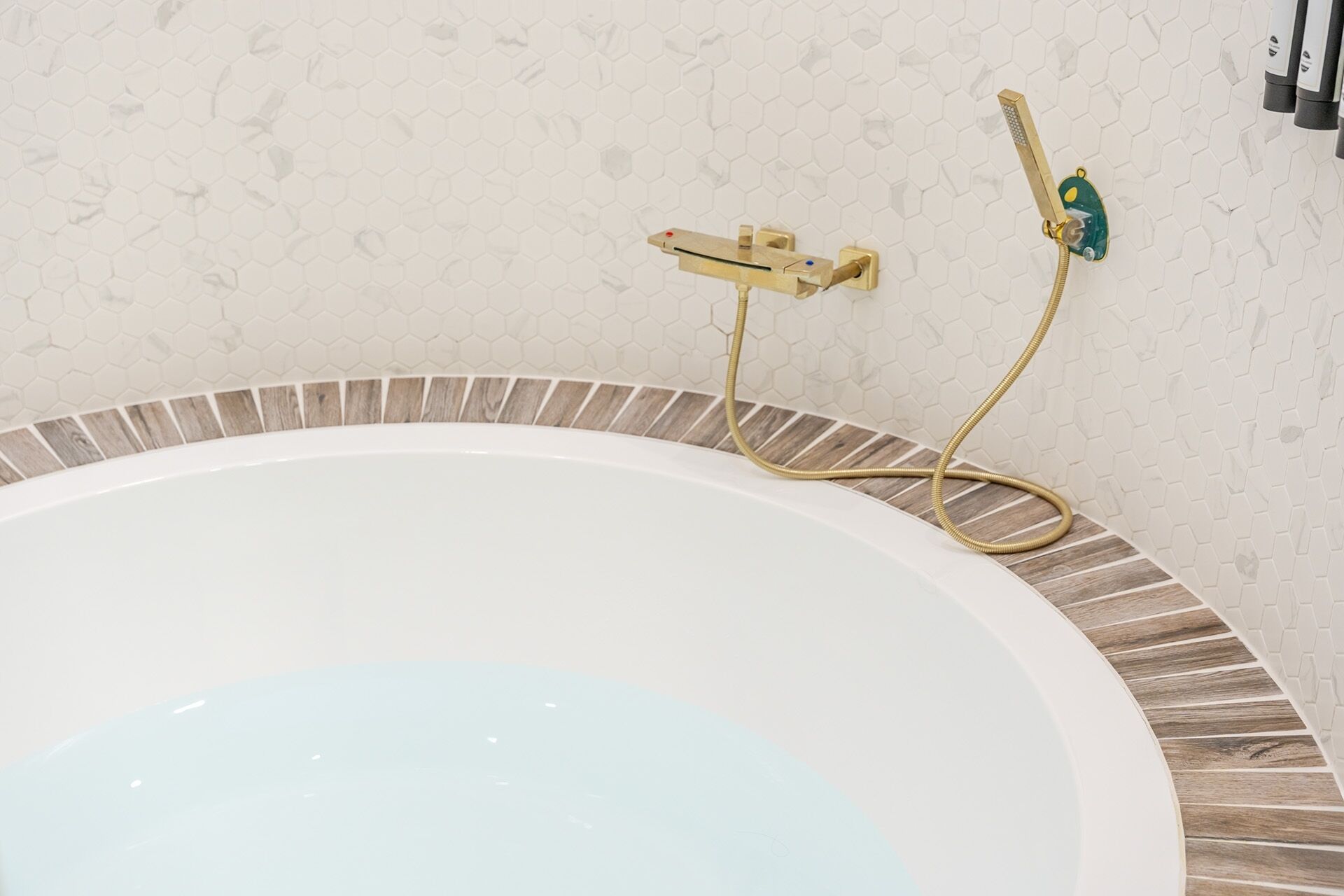 A bathtub with a wooden trim, a showerhead, and a control panel.